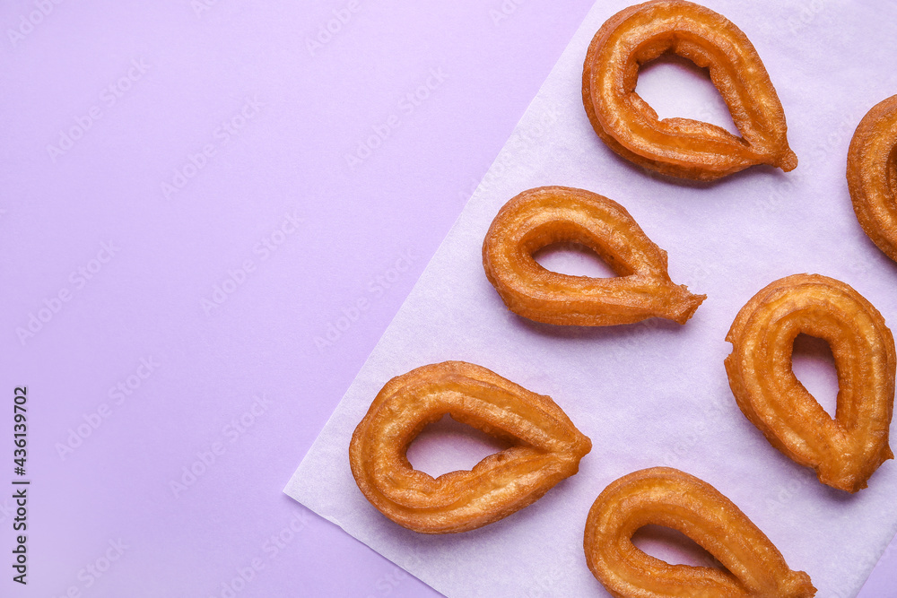 Parchment with tasty churros on color background