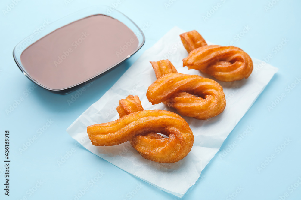 Parchment with tasty churros and melted chocolate sauce on color background