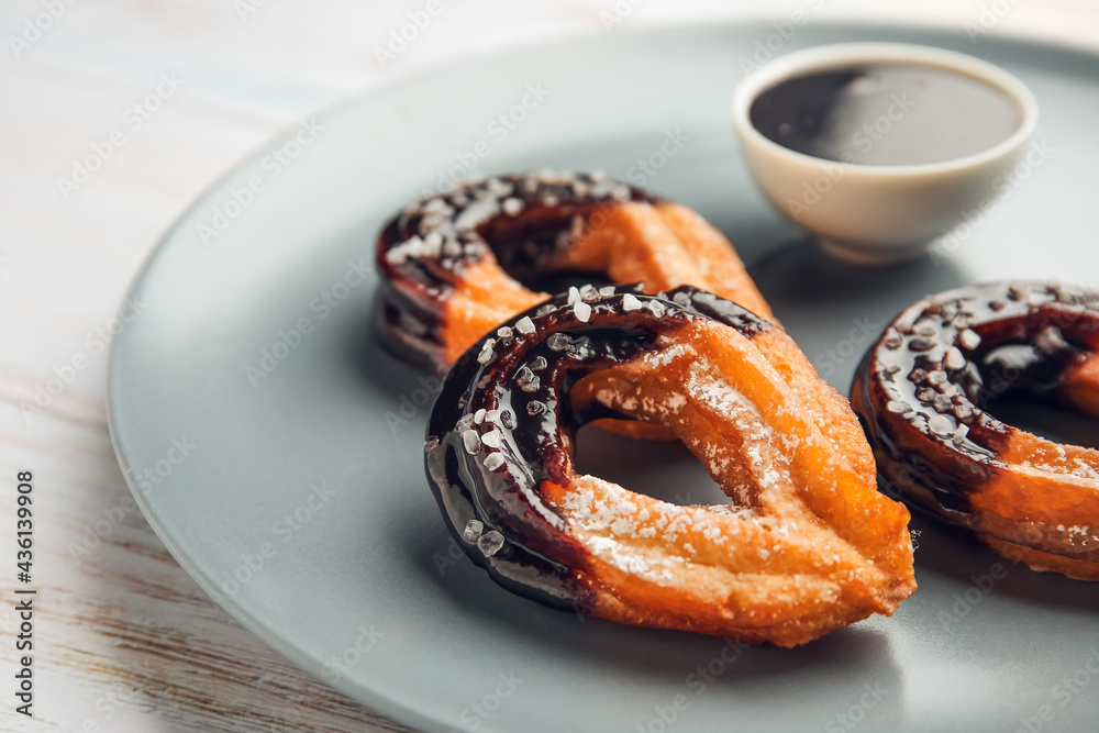 Plate with tasty churros dipped in chocolate on light wooden background, closeup