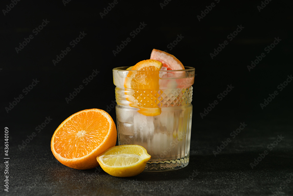 Glass of tasty cold lemonade and citrus fruits on dark background