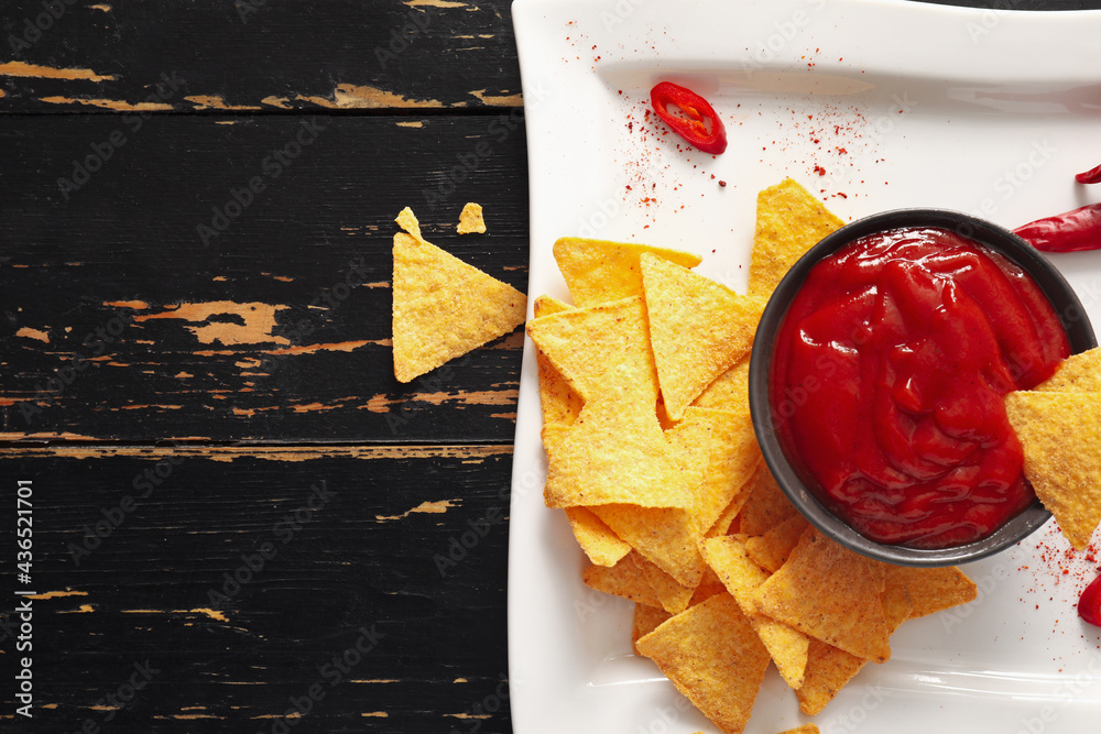 Tasty sauce, nachos and chili peppers on dark wooden background, closeup