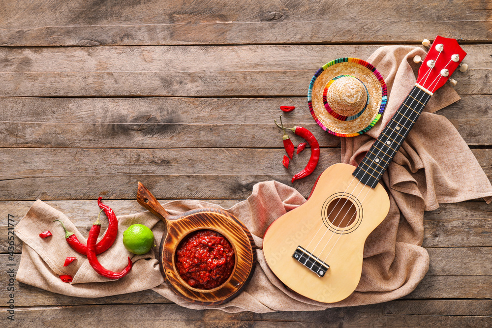 Composition with tasty chili sauce, ingredients, sombrero hat and ukulele on wooden background