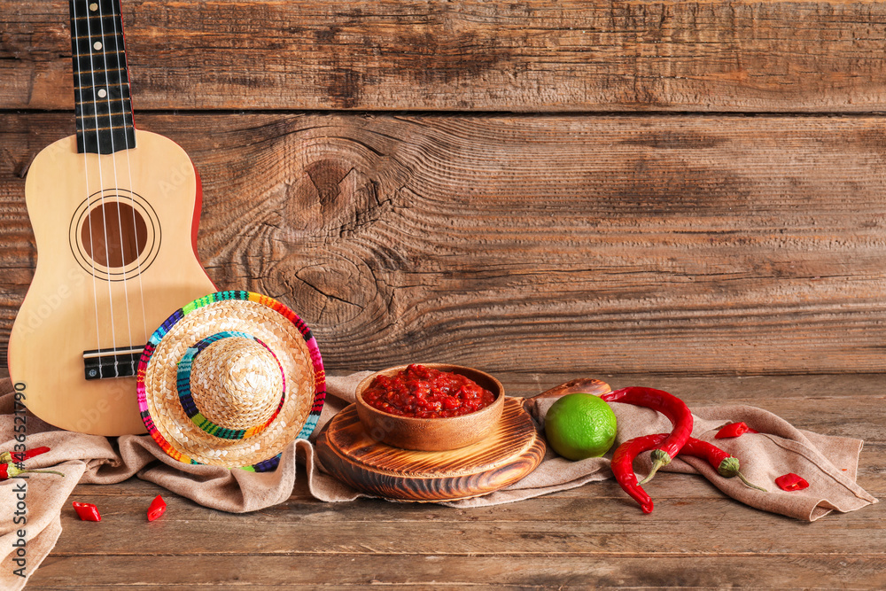 Composition with tasty chili sauce, ingredients, sombrero hat and ukulele on wooden background