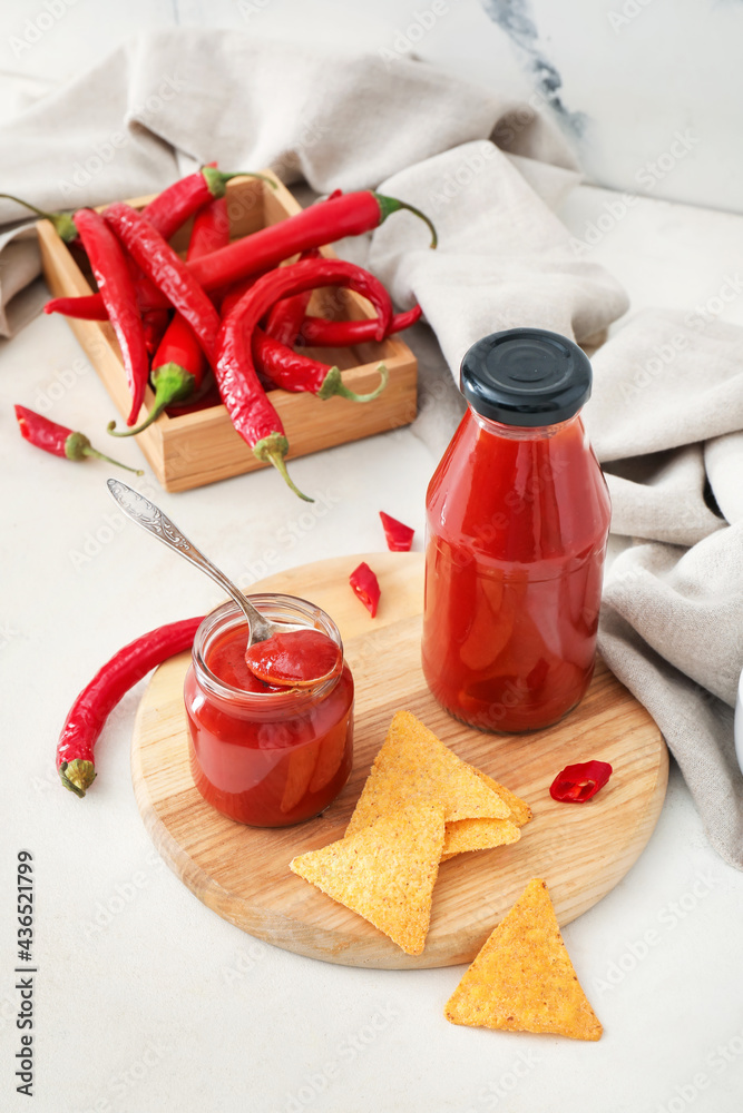 Tasty sauce, nachos and chili peppers on light background