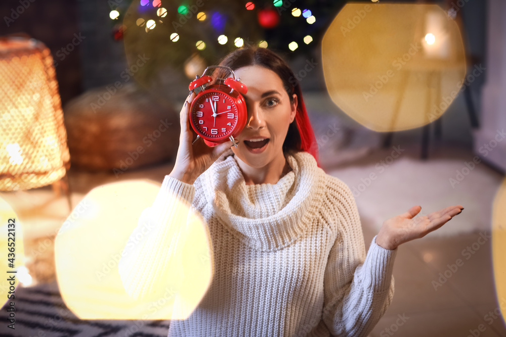 Surprised beautiful woman with alarm clock at home on Christmas eve