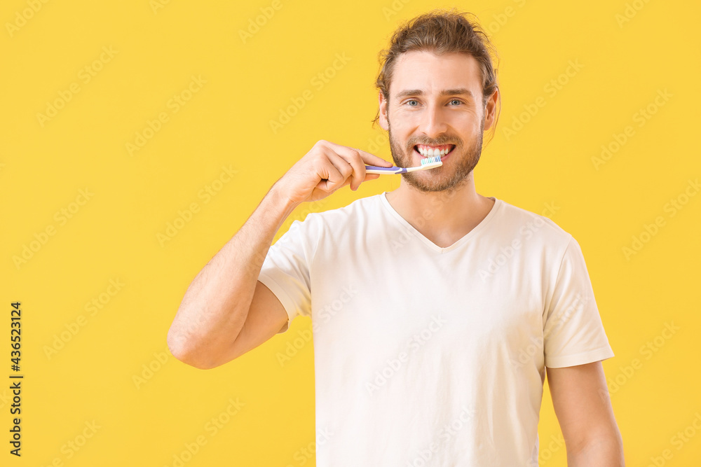 Young man brushing teeth on color background