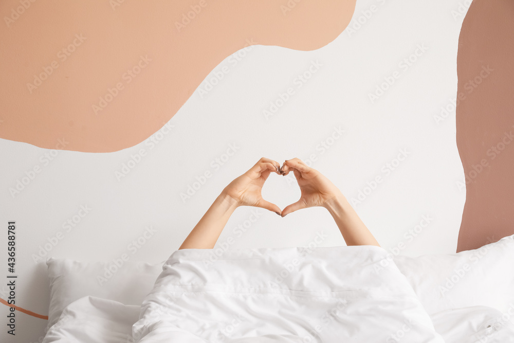 Young woman making heart with her hands in bedroom