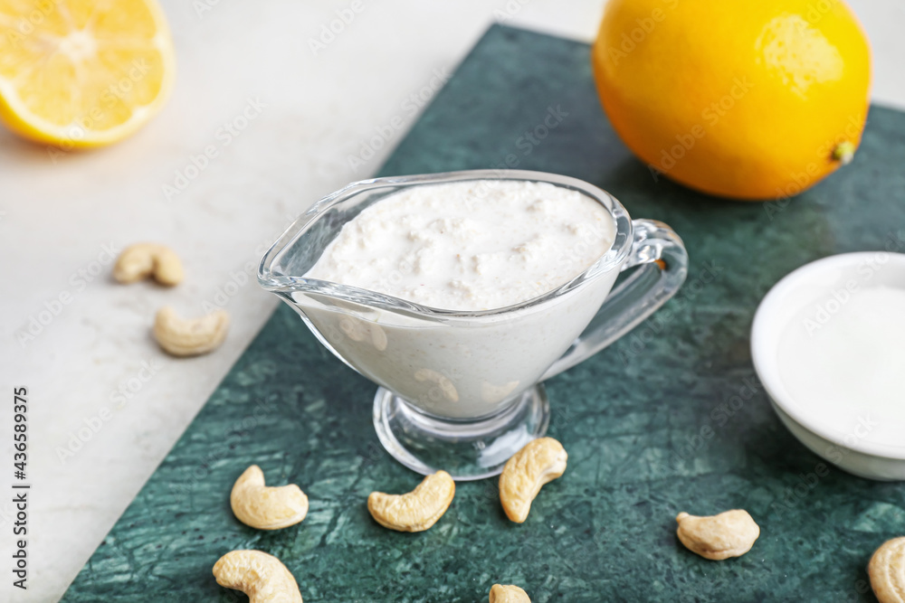 Gravy boat with cashew sour cream, nuts and lemon on light background