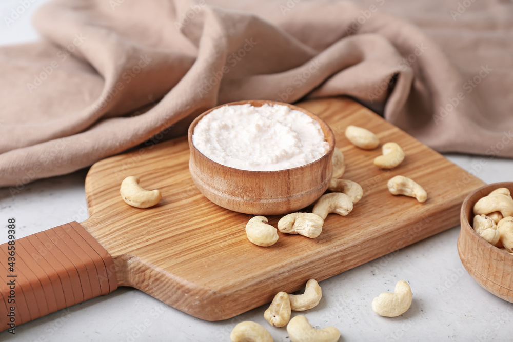 Bowl with cashew sour cream and nuts on light background