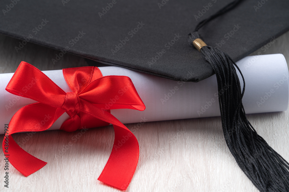 Graduation academic cap with diploma on wooden table background.