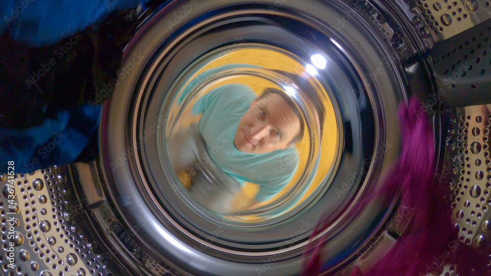 CLOSE UP, PORTRAIT: Man loads up the washer and watches it wash dirty laundry.