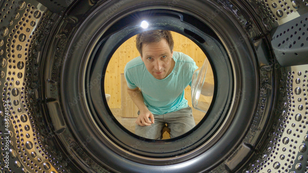 PORTRAIT: Smiling man opens the door and looks into the empty washing machine.