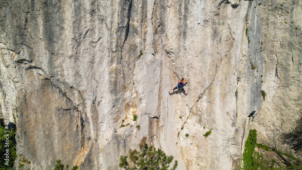 DRONE: Female climber learning to top rope looks for a hold in the natural wall.