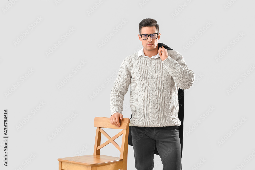 Fashionable young man with chair on grey background