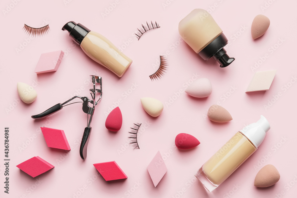 Makeup sponges with tonal foundation and eyelash curler on color background