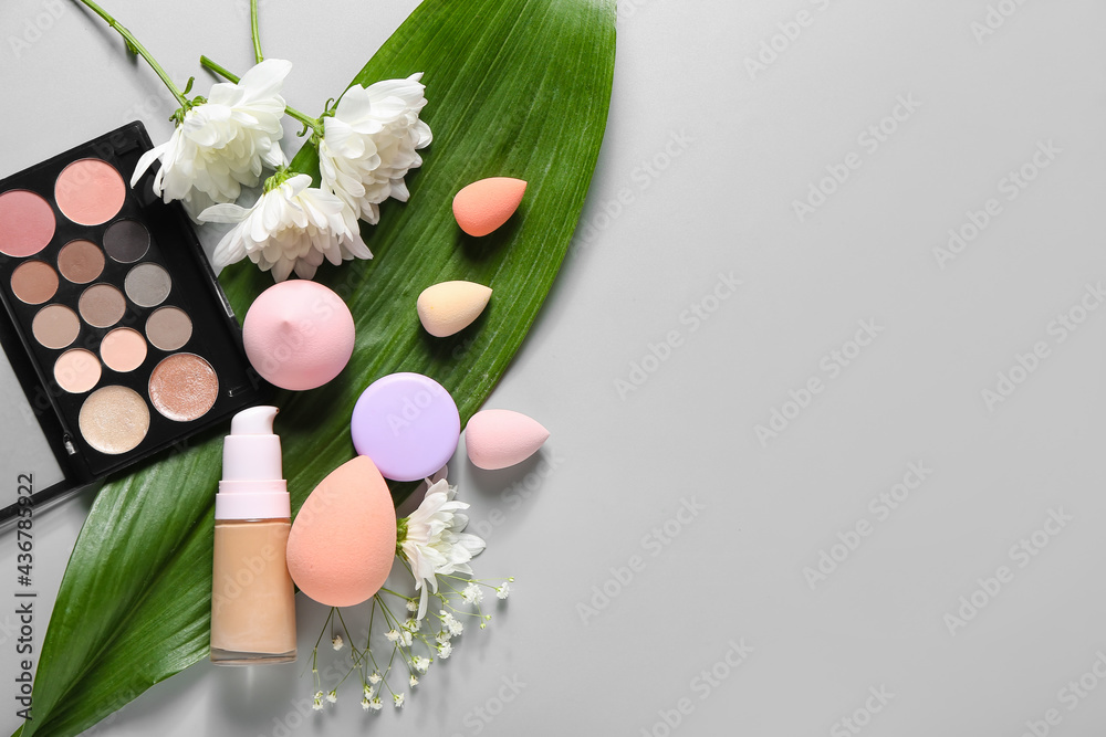 Composition with decorative cosmetics, makeup sponges and tropical leaf on color background