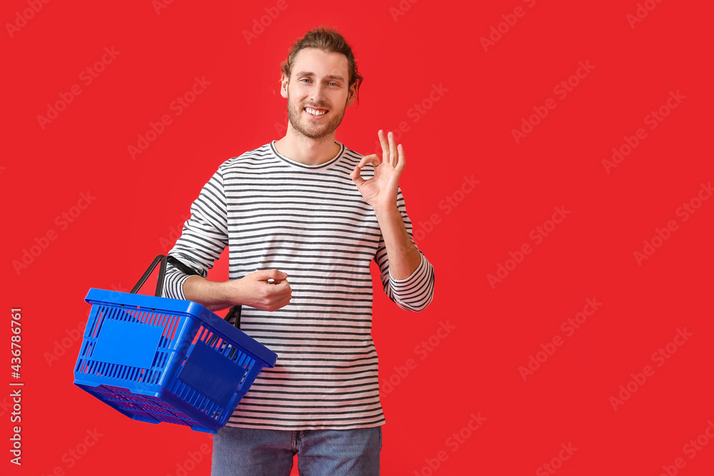 Young man with empty shopping basket showing OK on color background