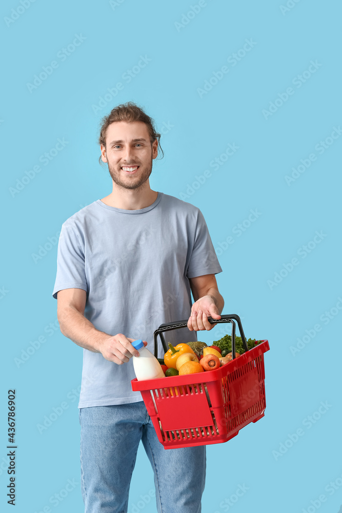 Young man with shopping basket on color background