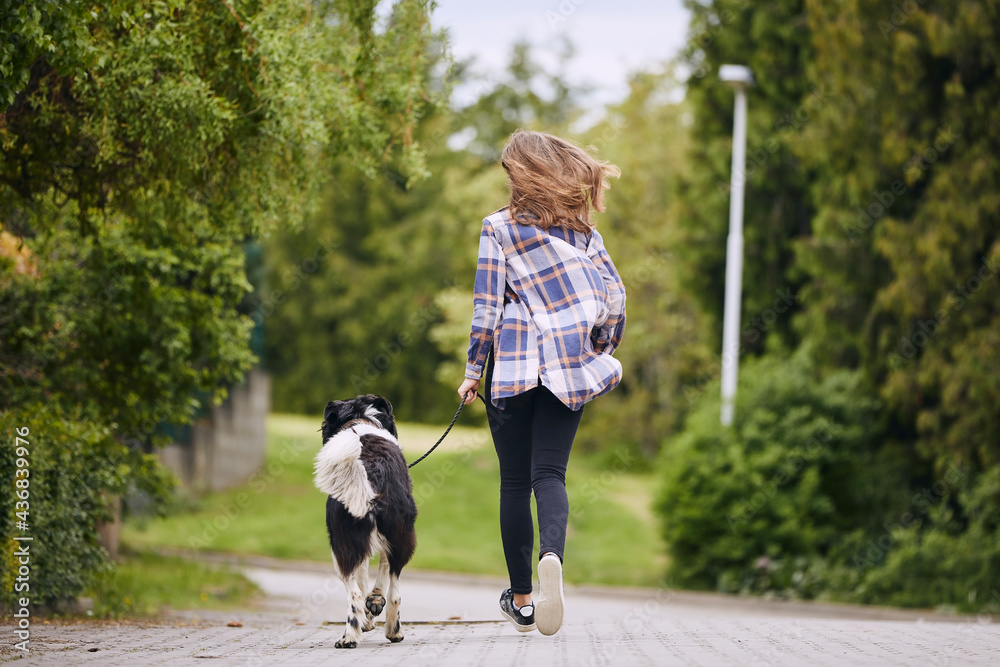 Rear view of teenage girl running with her dog on pet leash down street..