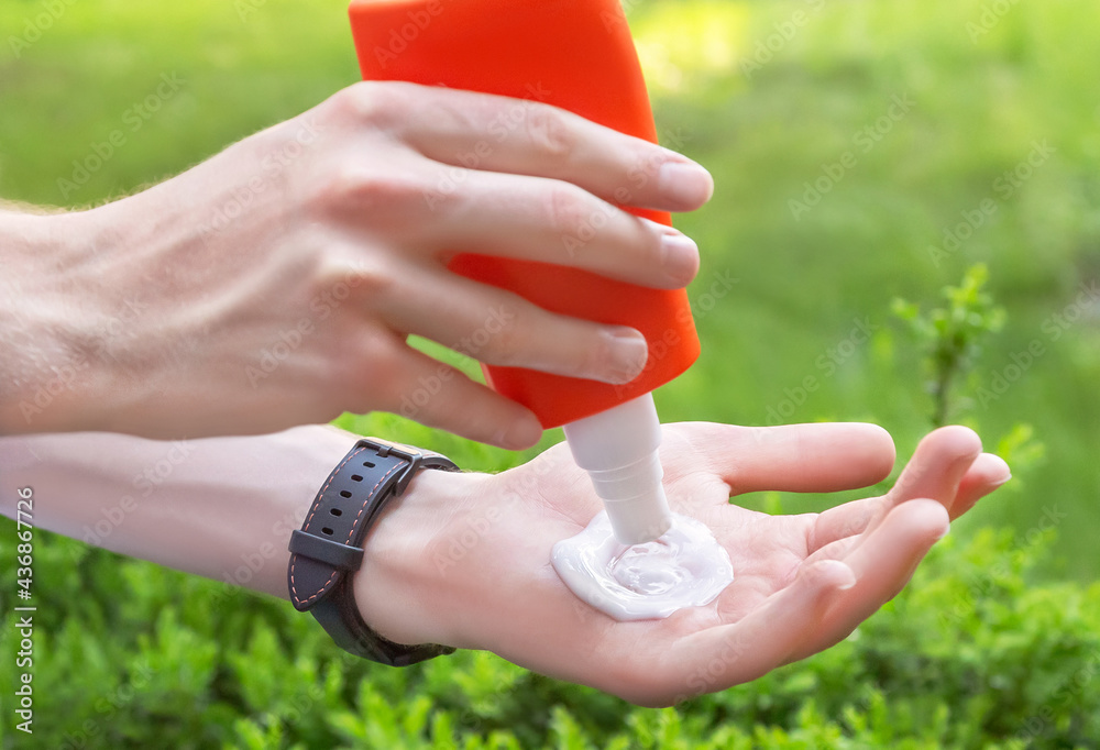 Sun protection. Caucasian mans hands with sunscreen (sun cream) plastic container on natural green 