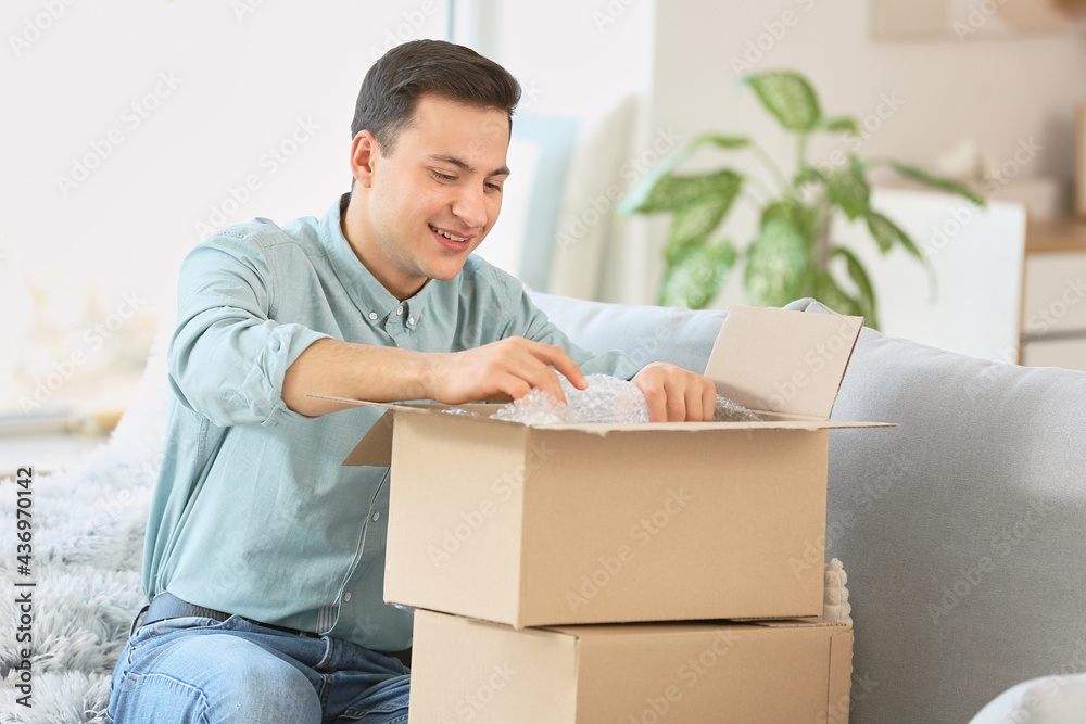 Happy young man unpacking parcel at home