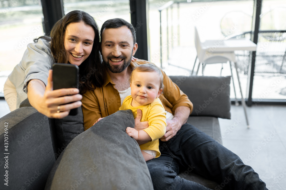 Happy family with a one year baby boy having a video call on phone from home. Concept of remote fami