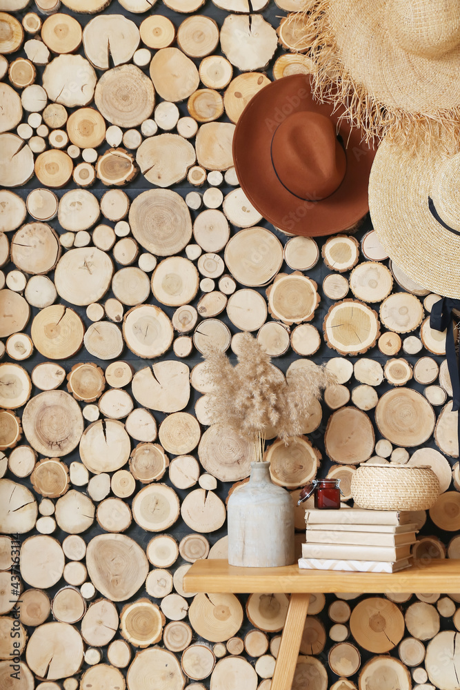 Bench with books and stylish hats hanging on wooden wall