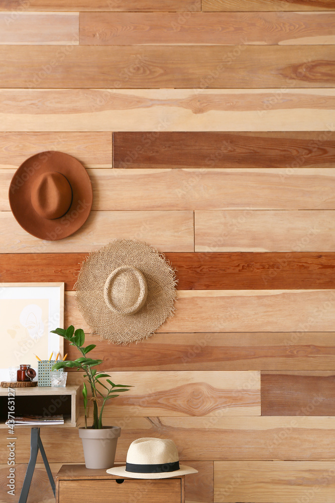 Table with houseplant and stylish hats hanging on wooden wall