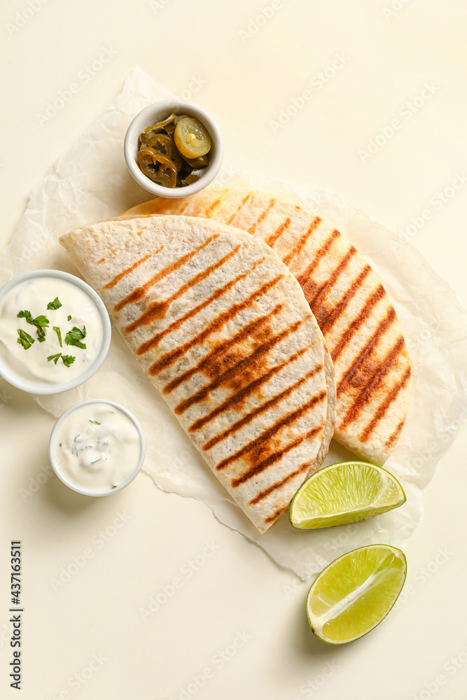 Parchment with tasty quesadillas, lime, sauces and pickled jalapenos on white background