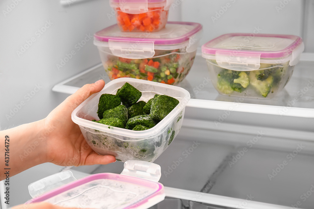 Woman with container of spinach in refrigerator