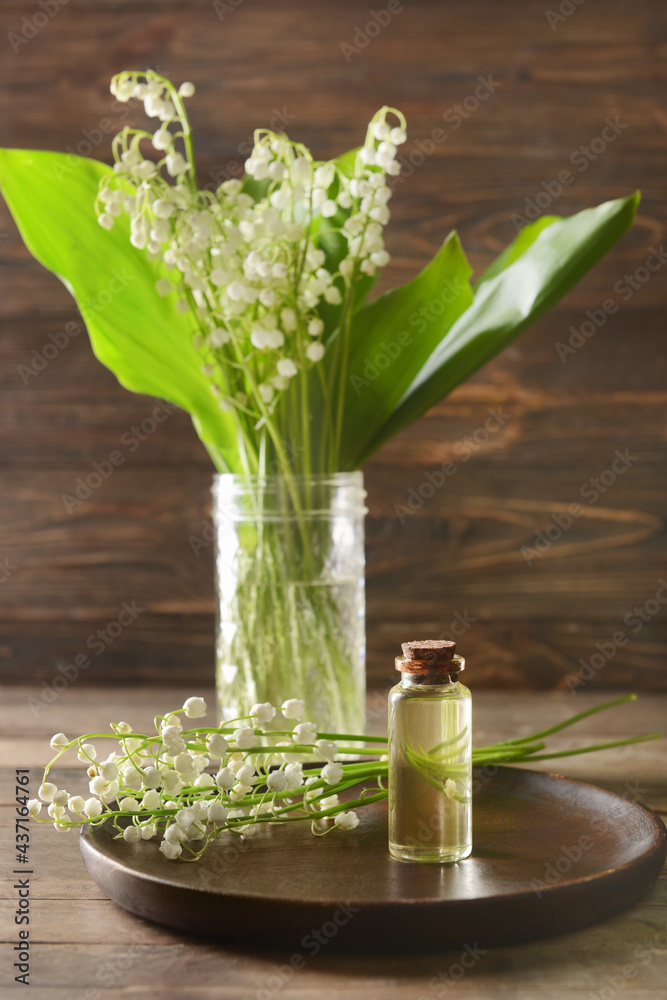 Bottle with essential oil and lily-of-the-valley flowers on wooden background