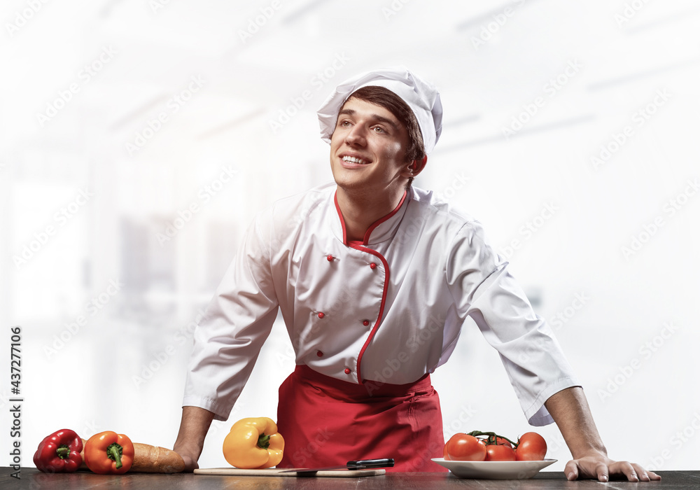 Young smiling chef standing near cooking table