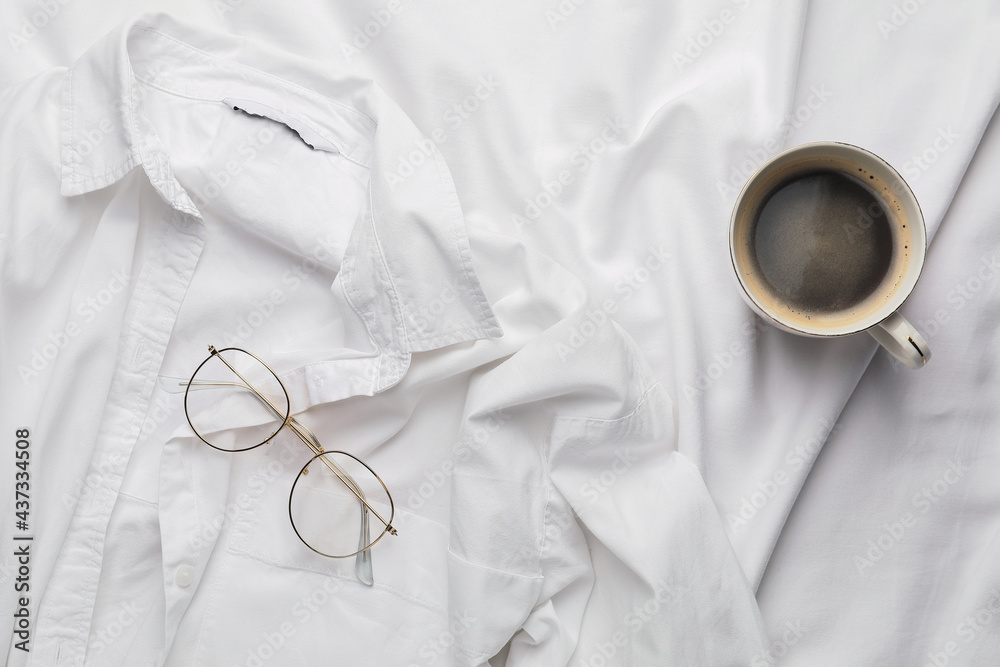 Cup of coffee with shirt and glasses on bed