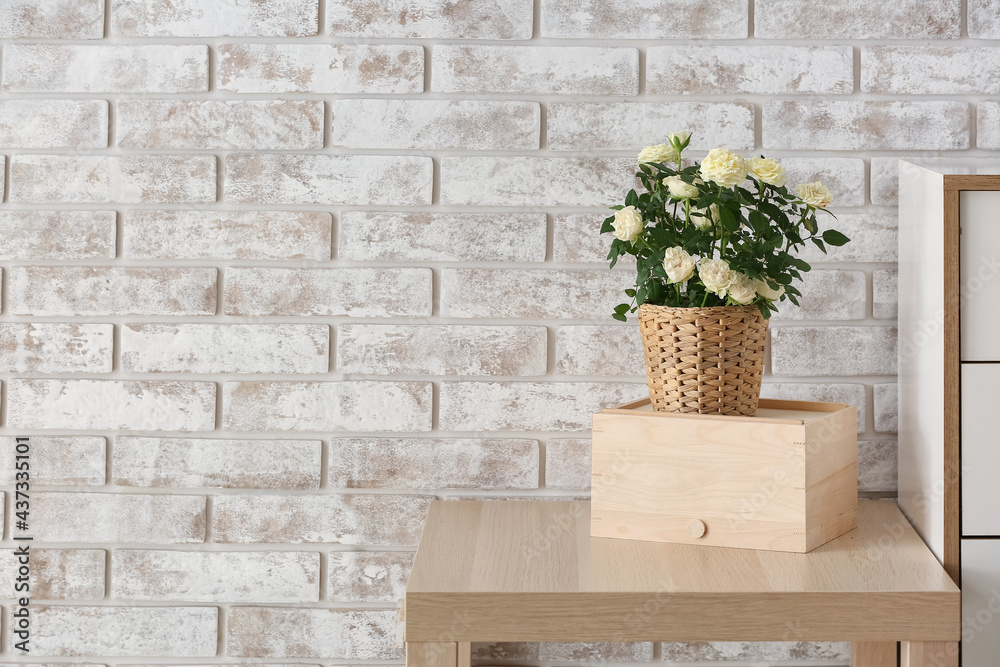 Beautiful white roses in pot on table near brick wall