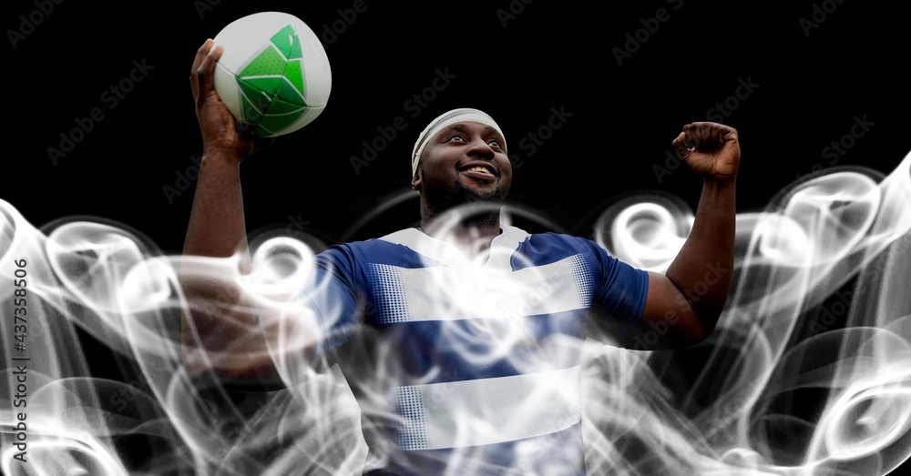 Compostion of african american rugby player holding ball on black background with white blur