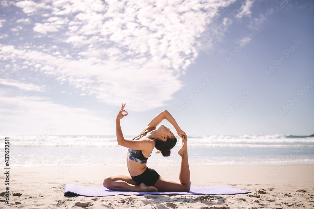 Woman doing one legged king pigeon pose on the beach