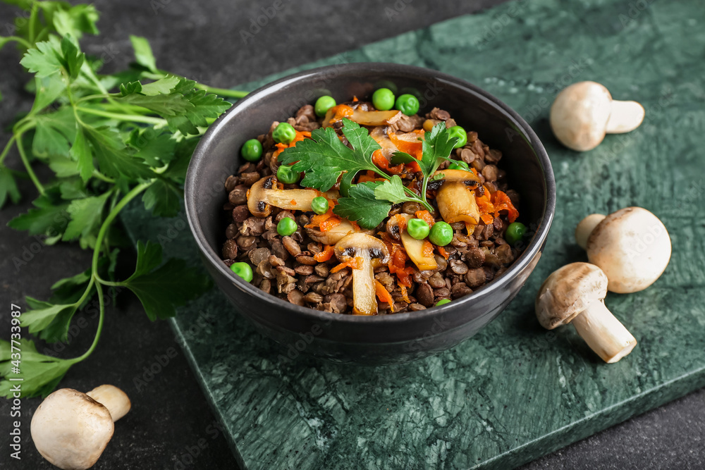 Bowl of tasty cooked lentils and mushrooms on dark background