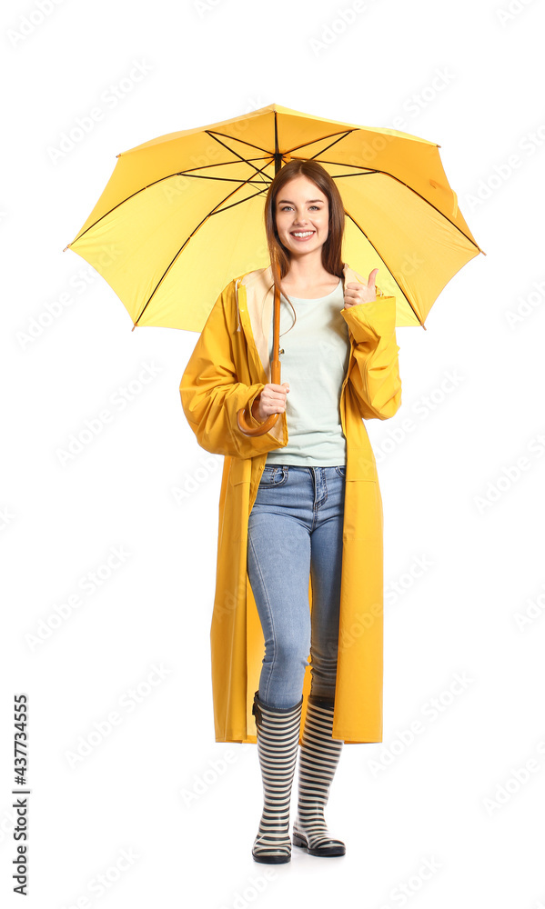 Stylish young woman in raincoat and with umbrella showing thumb-up on white background