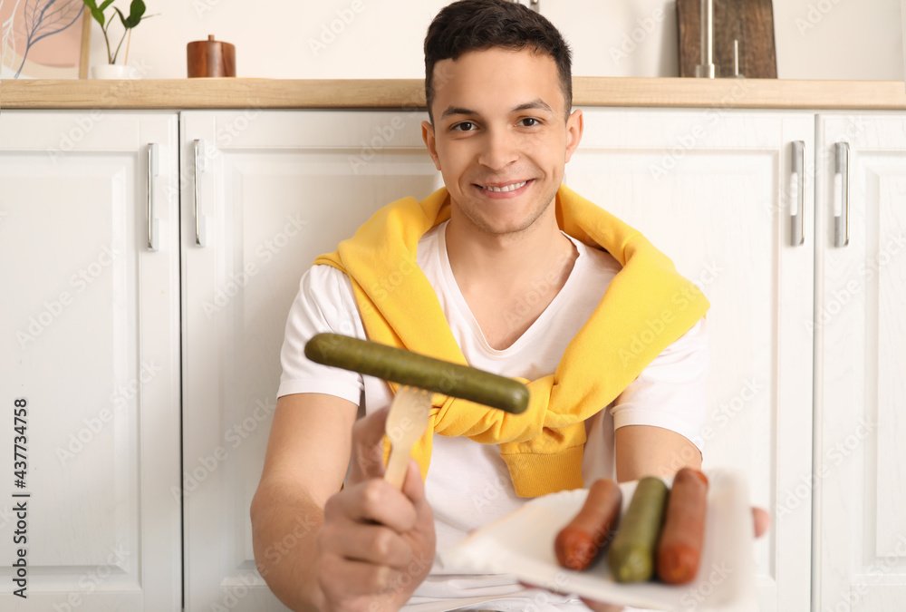 Young man with tasty sausages in kitchen