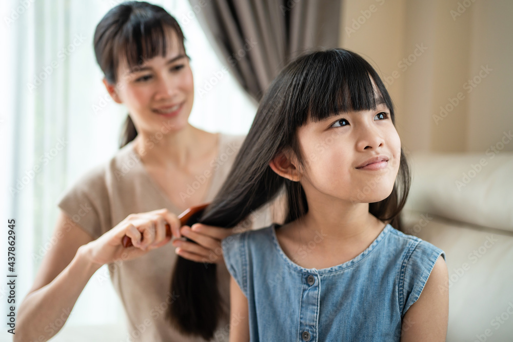 Parent mom comb little girl childs hair with hairbrush in living room