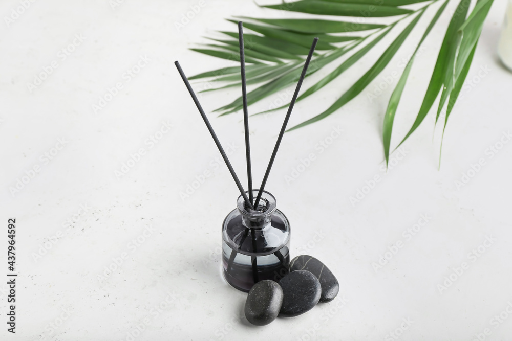 Reed diffuser with tropical leaf and spa stones on white background