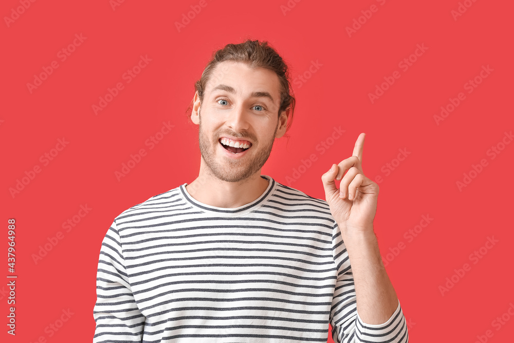 Smiling young man pointing at something on color background