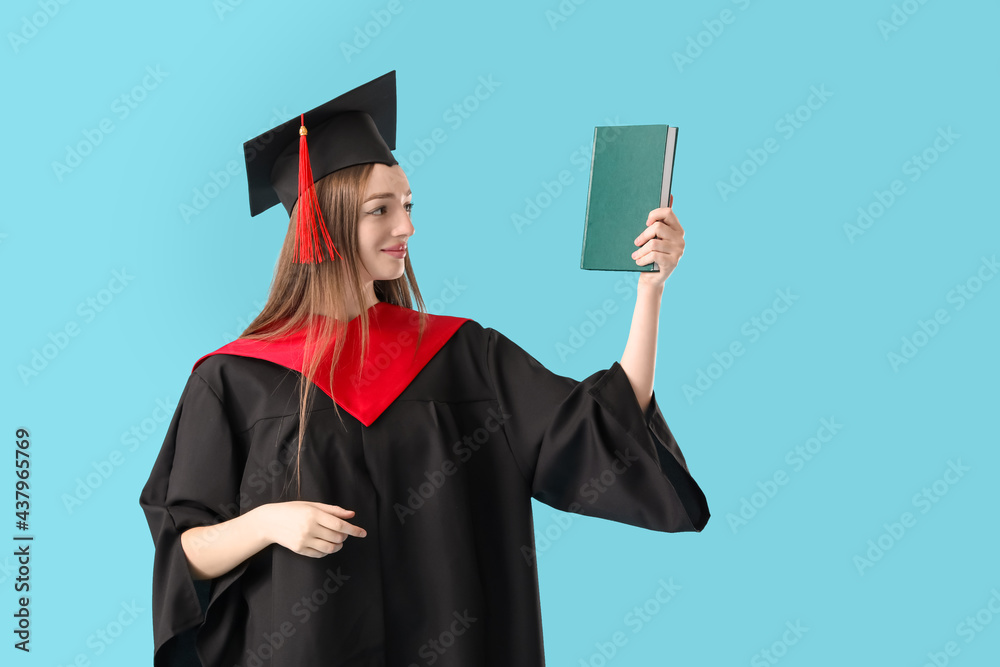 Female graduating student with book on color background