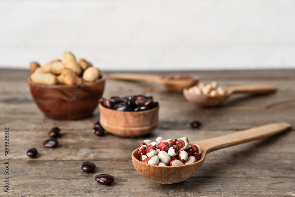 Bowls and spoons with different legumes on wooden background, closeup