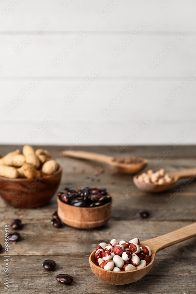 Bowls and spoons with different legumes on wooden background