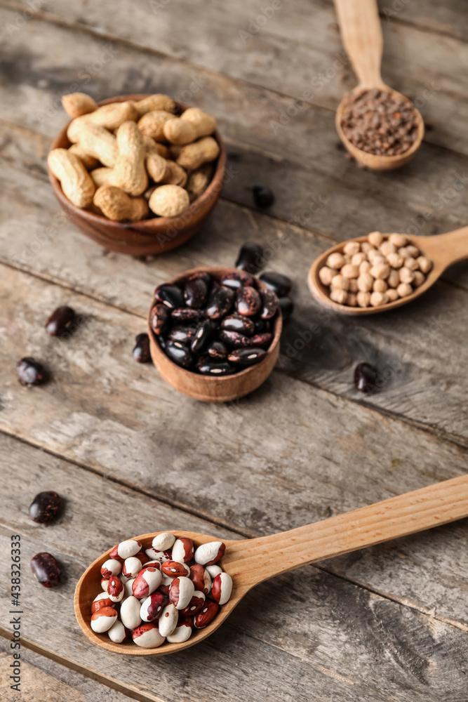 Bowls and spoons with different legumes on wooden background