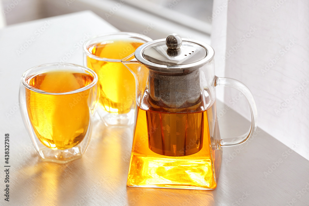 Teapot and cups of hot beverage on table in room