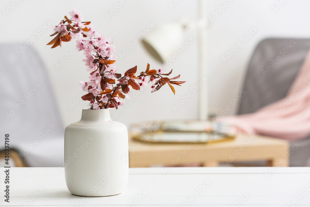 Vase with beautiful blossoming branches on table in room