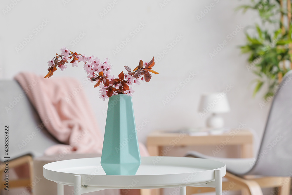 Vase with beautiful blossoming branches on table in room