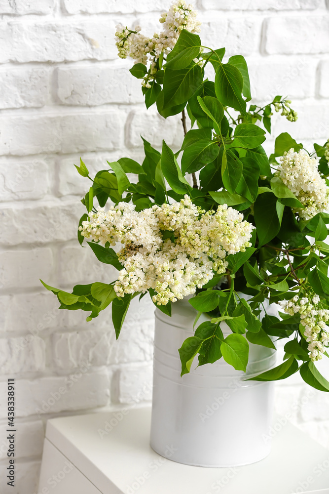 Vase with lilac flowers on table near brick wall